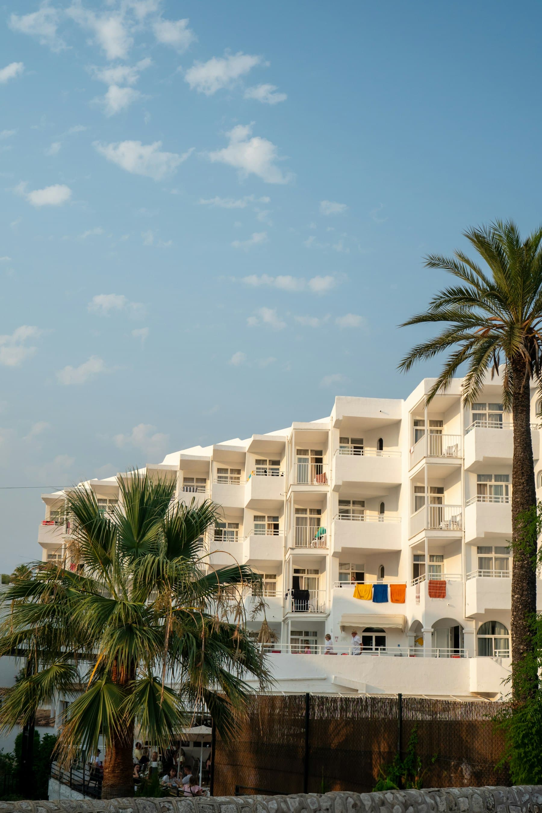 Fachada de hotel mediterráneo con palmeras bajo un cielo azul